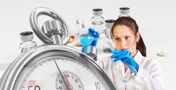 une laborantine effectue un mélange derrière un chronomètre en premier plan